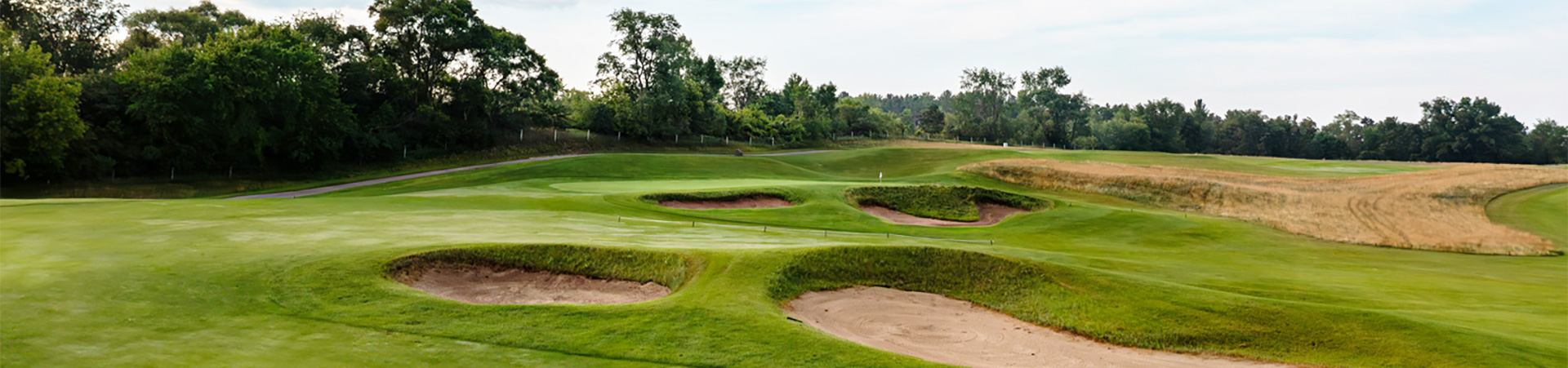 A scenic view of a golf course featuring sand traps, lush green grass, and trees in the background.